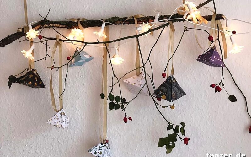 Adventskalender basteln – selbst gemachte Papierpyramiden hängen an einem Ast mit Lichterkette.