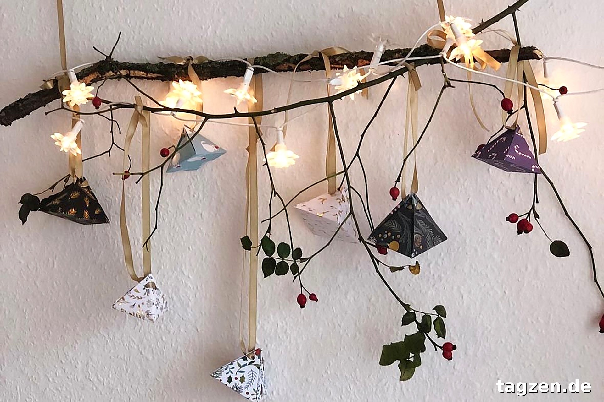 Adventskalender basteln – selbst gemachte Papierpyramiden hängen an einem Ast mit Lichterkette.